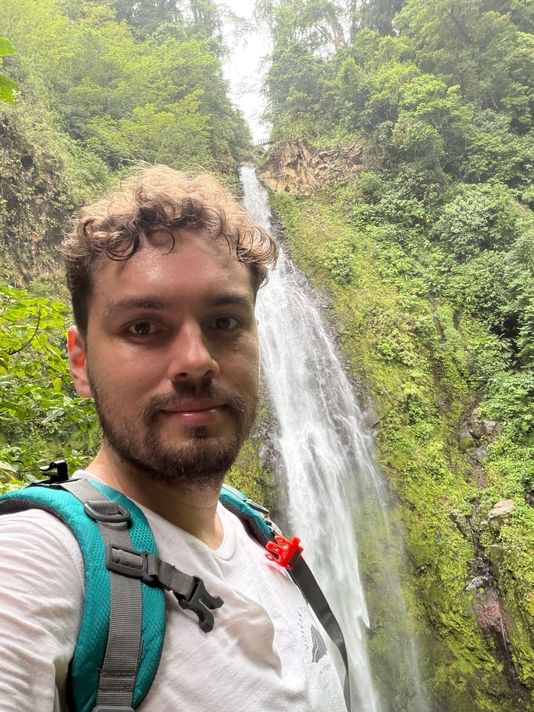 Jose on a hiking trail at the foot of a tall rainforest waterfall